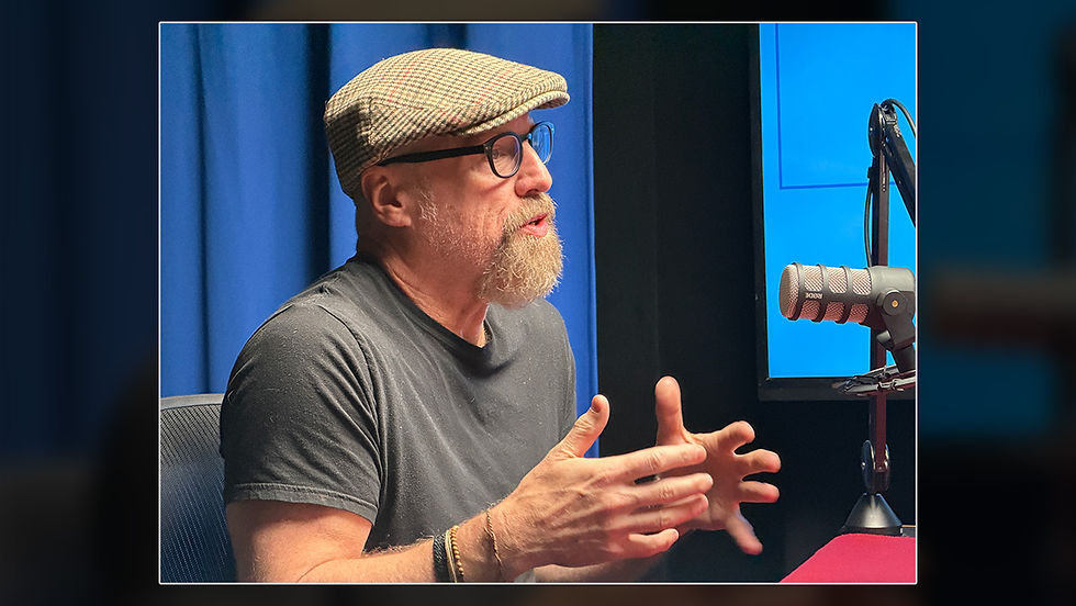 Meg Bell interviews local author Doug Crandell for the Pages & Voices podcast. Crandell reads from a book while seated across from Bell in a podcast recording studio.