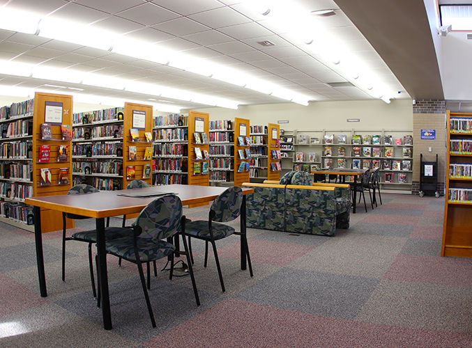 Library interior with rows of bookshelves, desks with chairs, and cushioned seating.
