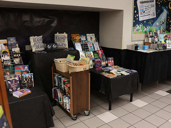 Books with vibrant covers displayed on black-covered tables and carts in a library.