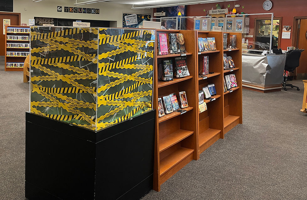 Library scene with two wooden bookshelves partially filled with books, and a display blocked off with yellow ‘Under Construction’ tape for Halloween.