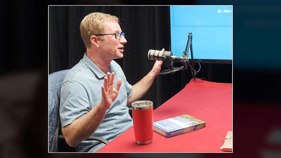Meg Bell interviews local author Kelsey Timmerman for the Pages & Voices podcast. Timmerman gestures while speaking across a table equipped with microphones in a recording studio.