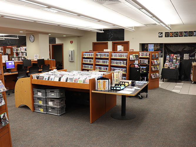 Interior of a library featuring wooden bookshelves of DVDs and CDs, along with several computer stations.
