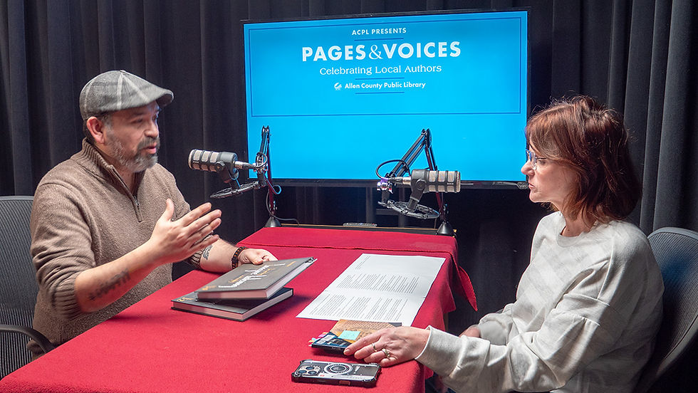 Meg Bell interviews local author Ricardo Martinez for the Pages & Voices podcast. Martinez speaks while Bell listens across a table with books, notes, and microphones.