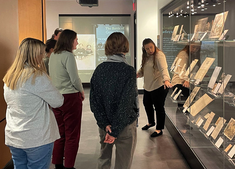 Museum tour group viewing historical documents in glass display case.
