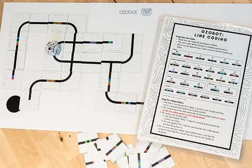 Ozobot coding activity with a programmable robot, track tiles, and color-coded line coding guide.