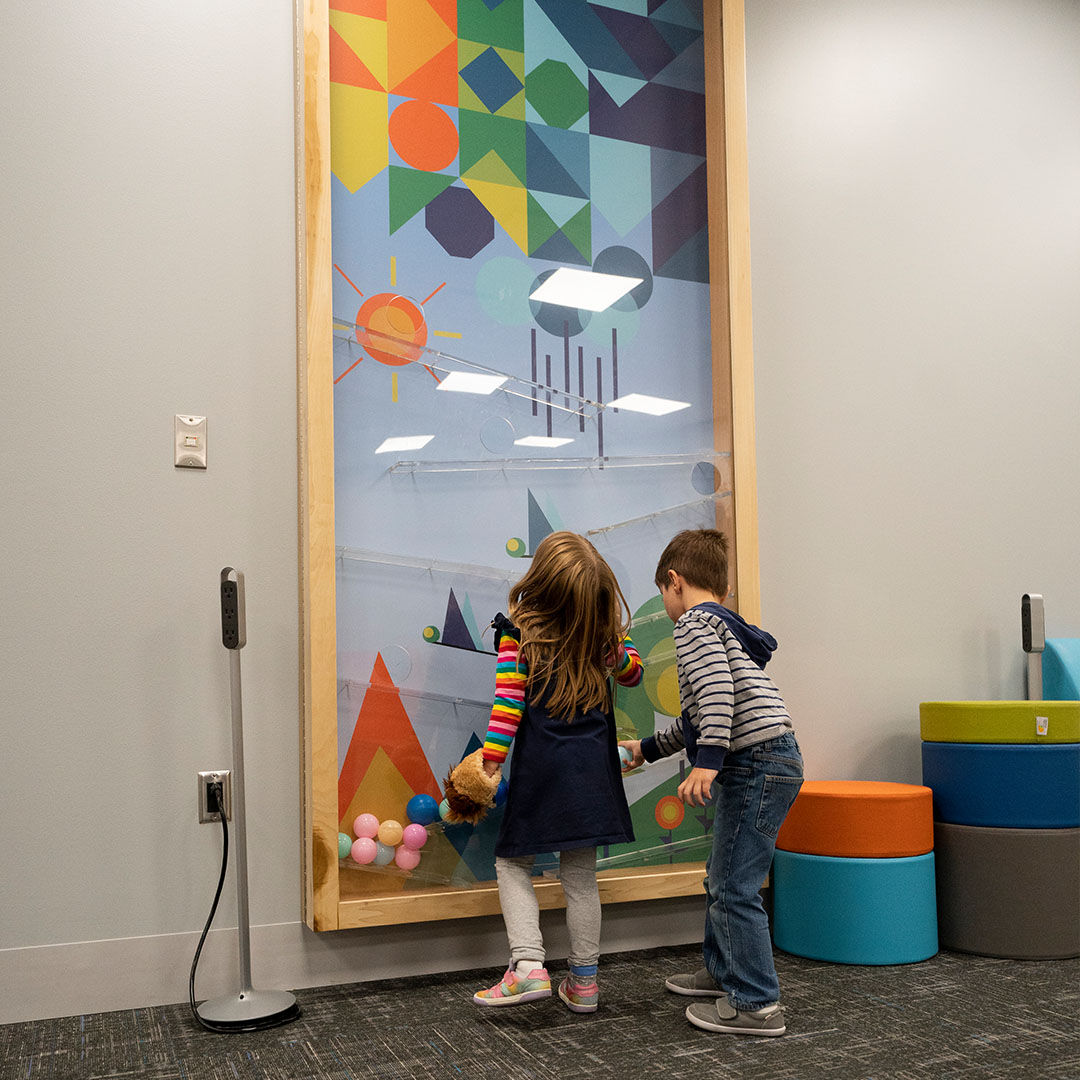 Two children in the Storyscape area explore a colorful interactive wall with geometric shapes.