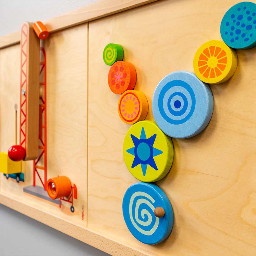 Colorful interactive play wall with vibrant wooden gears and shapes featuring spirals and stars.