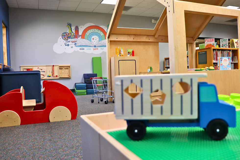 StoryScape area at Pontiac Branch with colorful furniture, a mini shopping cart, large wooden play structures, and a vibrant StoryScape mural on the back wall.
