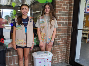 Two girl Scouts stand next to a collection bin for their Community Hygiene Drive