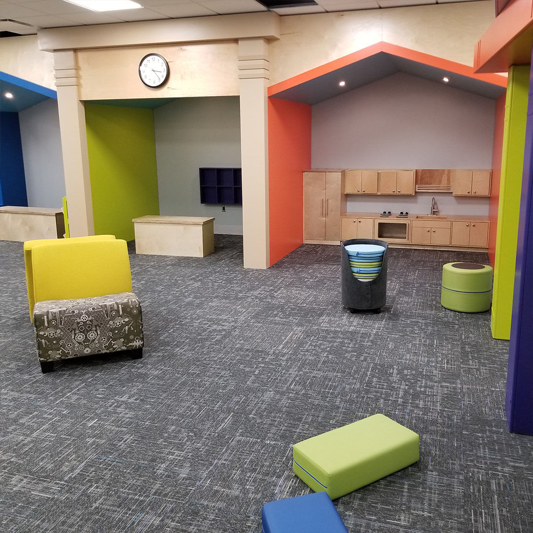 A spacious, colorful Storyscape area with house-shaped play areas, vibrant furniture, and educational toys.