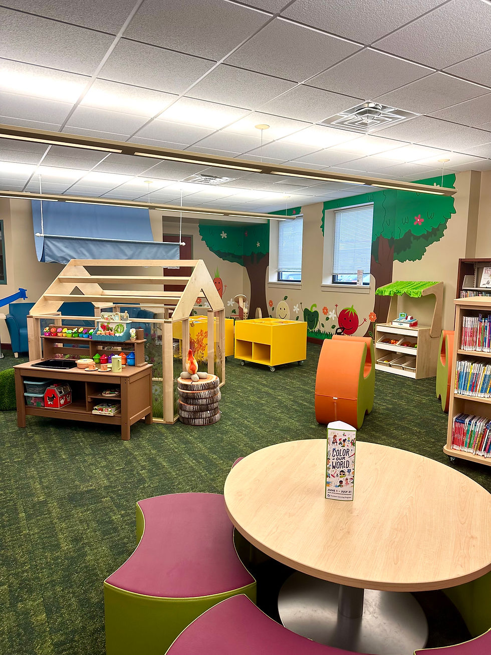 StoryScape area at Little Turtle Branch with a play greenhouse, play kitchen, play farmer’s market stand, and wall murals of trees and Seed Library characters.