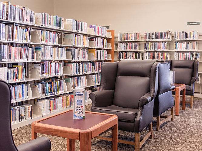 The adult fiction section with plush black leather chairs, wooden tables, and bookshelves filled with books.