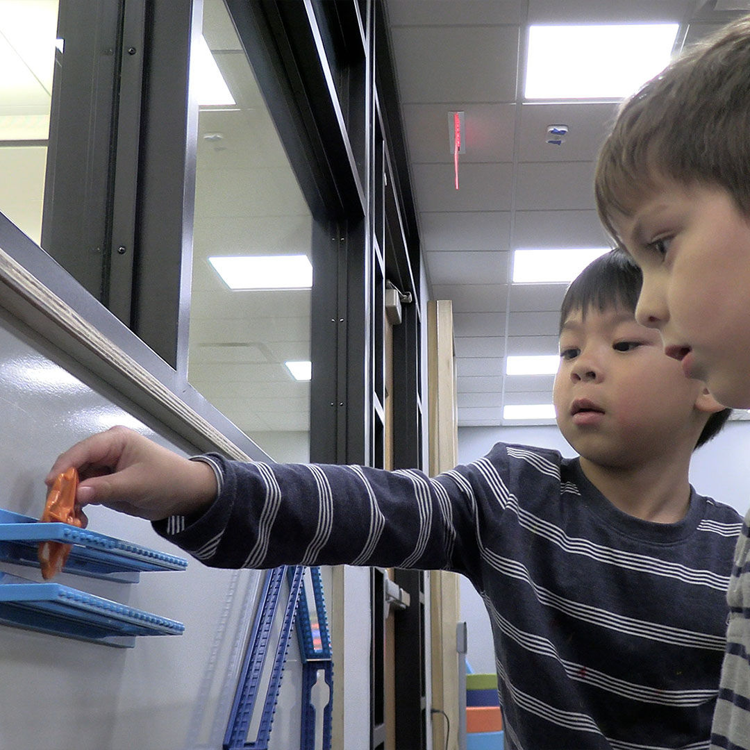 Two young children in striped shirts play with an interactive wall in the Storyscape area, focusing and collaborating closely.
