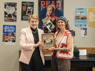 Susan Baier and Grace Yencer hold Grace's Dolly Parton print in front of a Dolly Parton Read poster.