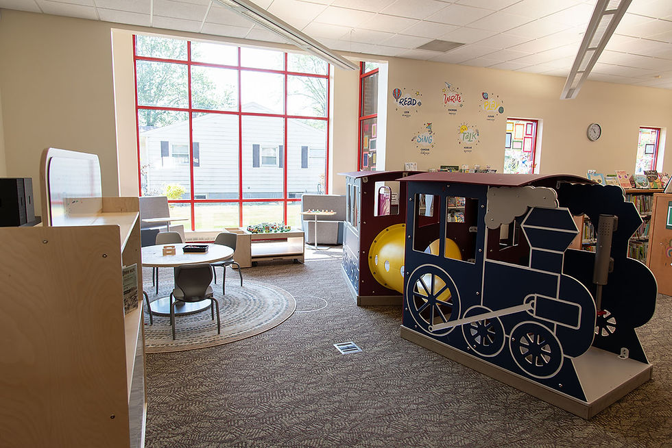 StoryScape area at Grabill Branch featuring large windows, a round table with chairs, and a train play structure.