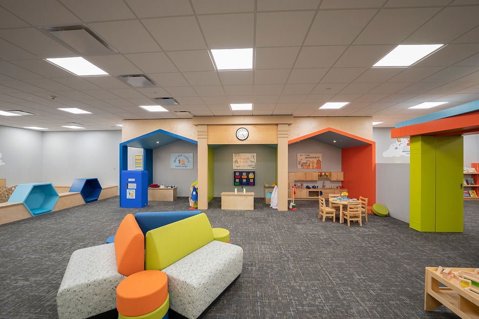 StoryScape area at Main with interactive playhouses, toys, small tables and chairs, and colorful furniture on a carpeted floor.