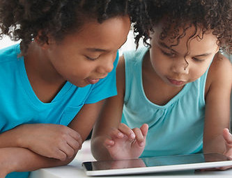 Two young girls looking at a tablet together, focused, learning, and interacting.