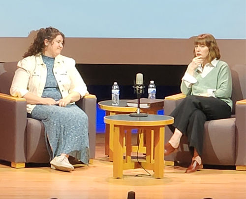 Dos mujeres conversando en el escenario de la biblioteca frente a un micrófono.