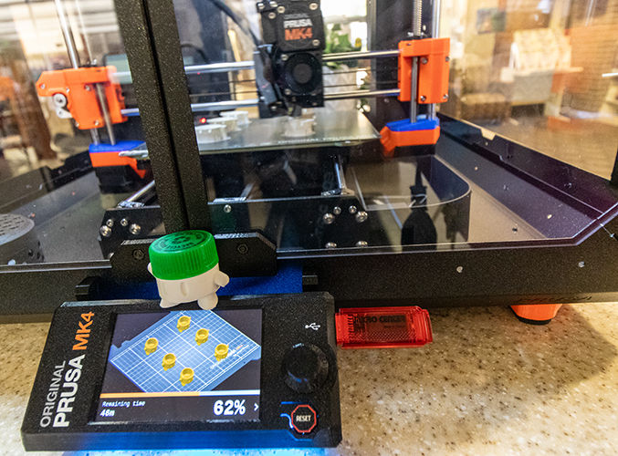 Impresora 3D en funcionamiento con una pantalla digital que muestra el progreso y un diseño complejo en la pantalla.
