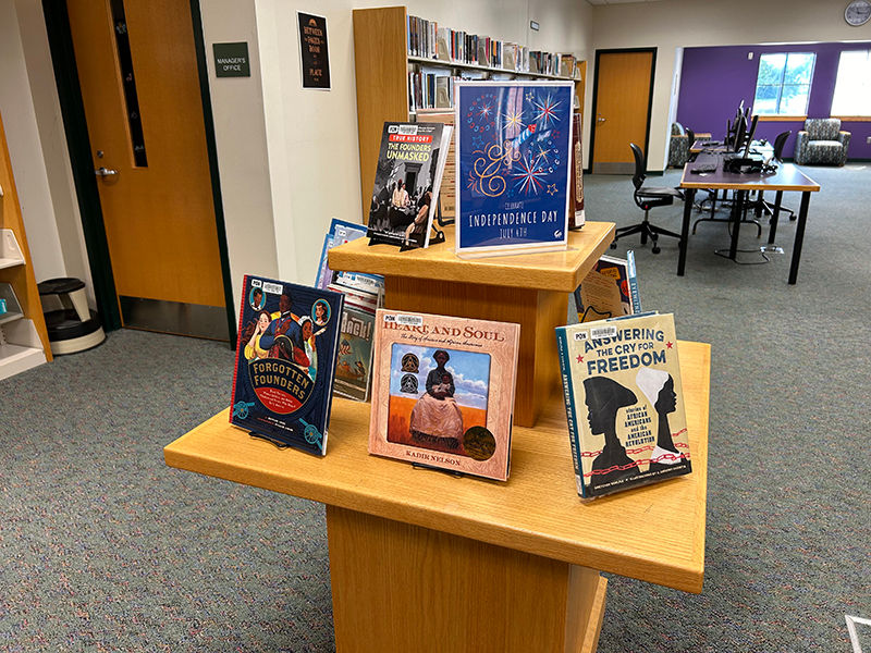 Exhibición de libros de madera en una biblioteca, con libros sobre el Día de la Independencia.