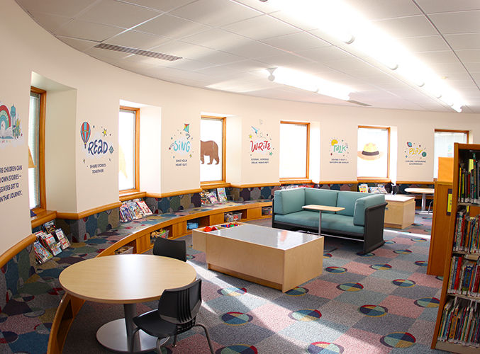 Children’s Storyscape section with colorful wall art, circular seating, low curved-wall seating with books in cubbies, and playful carpet patterns.