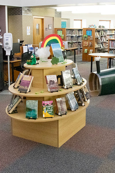 Library display with three-tiered shelves of books, decorated with a rainbow and shamrocks for a St. Patrick’s Day theme.