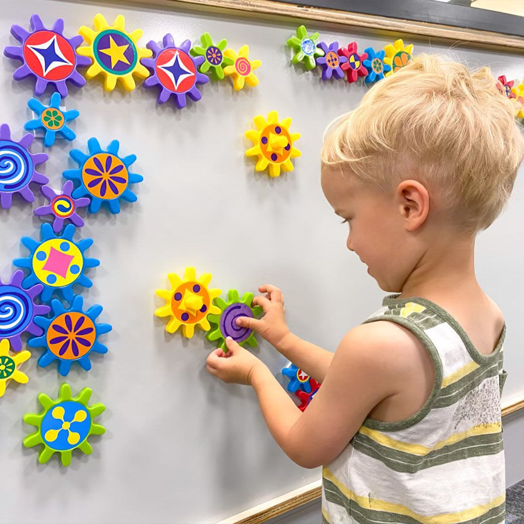 A child playing with colorful interlocking gear toys on a wall, featuring vibrant patterns and shapes.