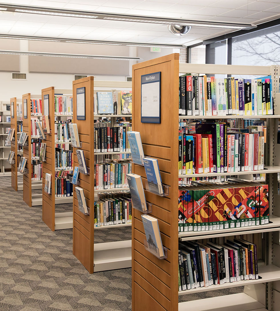 Interior de la biblioteca con pasillos de estanterías repletas de libros coloridos y separadores de madera que exhiben los libros destacados.