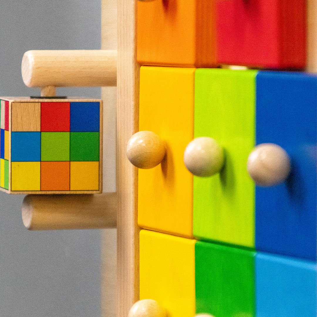 Close-up of a colorful wooden toy with square blocks in red, orange, yellow, green, and blue, each featuring a small round wooden knob.