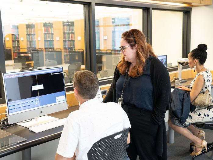 Library employee helps a patron doing research at a computer.