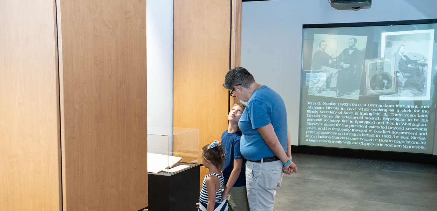 Familia observando una exposición con imágenes y texto en la Biblioteca Pública del Condado de Allen.