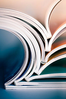 Varias revistas abiertas y apiladas unas dentro de otras, desplegadas en forma de abanico sobre una mesa.