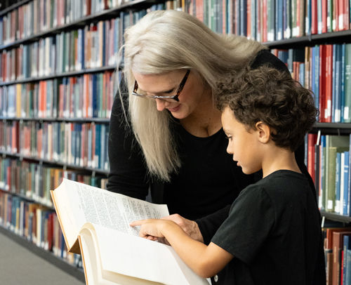 ACPL Staff member helping a young patron look something up in a book