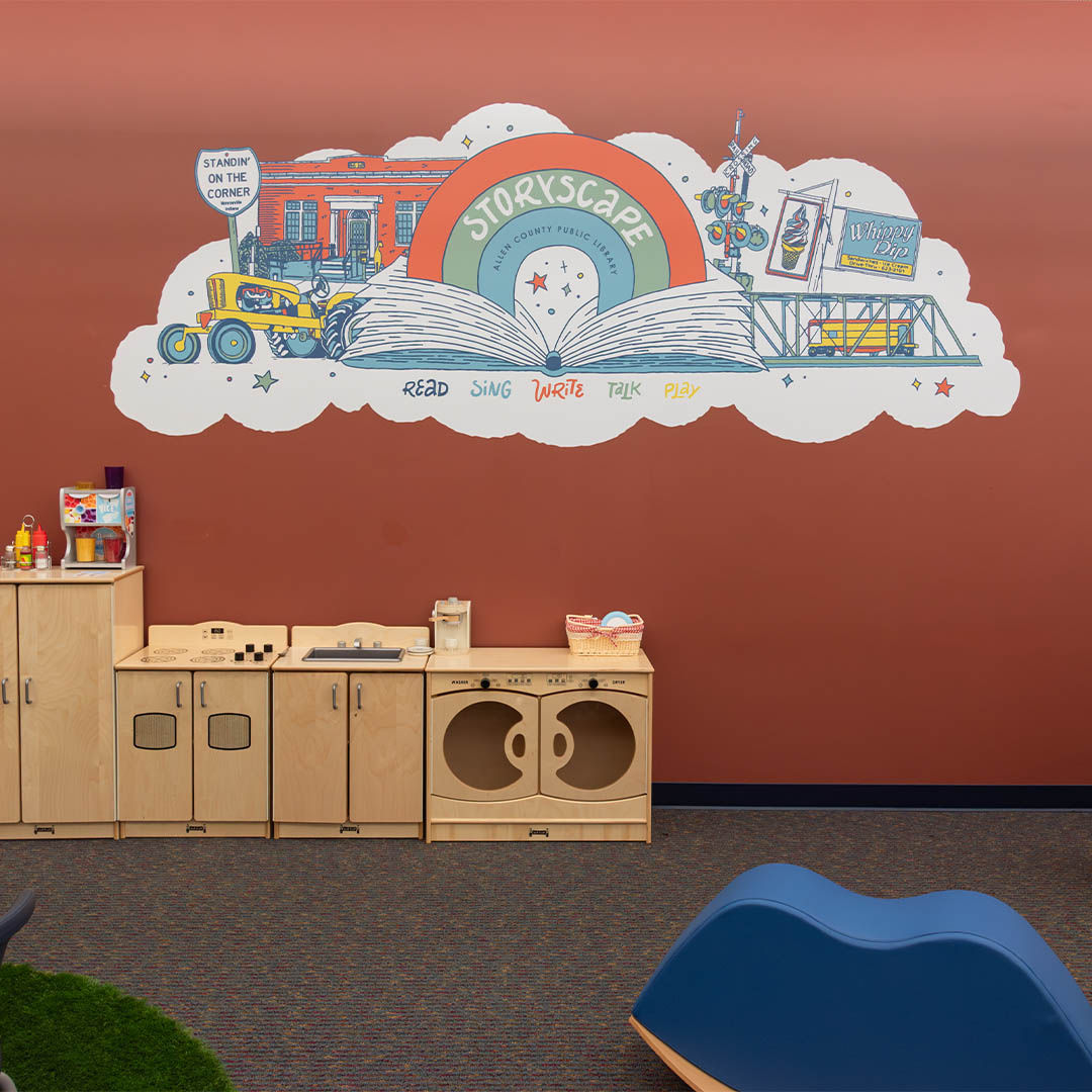 The Storyscape area featuring a colorful mural with the words StoryScape and whimsical scenes. A wooden play kitchen is in front.