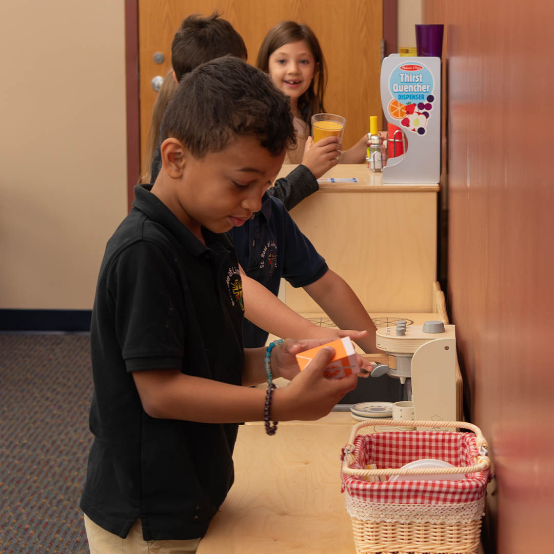 Children play in a kitchen play area, engaging with a pretend juice dispenser and toy groceries, appearing focused and cheerful.