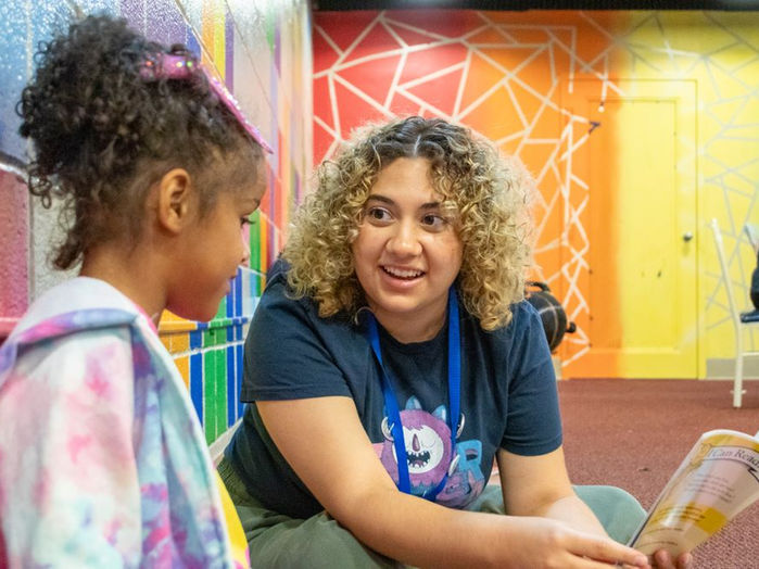 A teen working with Team Read, reads a book to a younger girl.